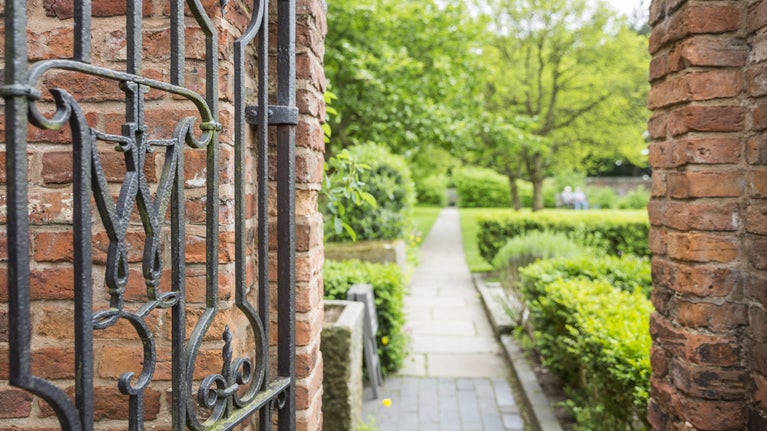 A view of the garden at Moseley Old Hall framed by an iron gate, with a pathway, box hedges and trees visible in the garden